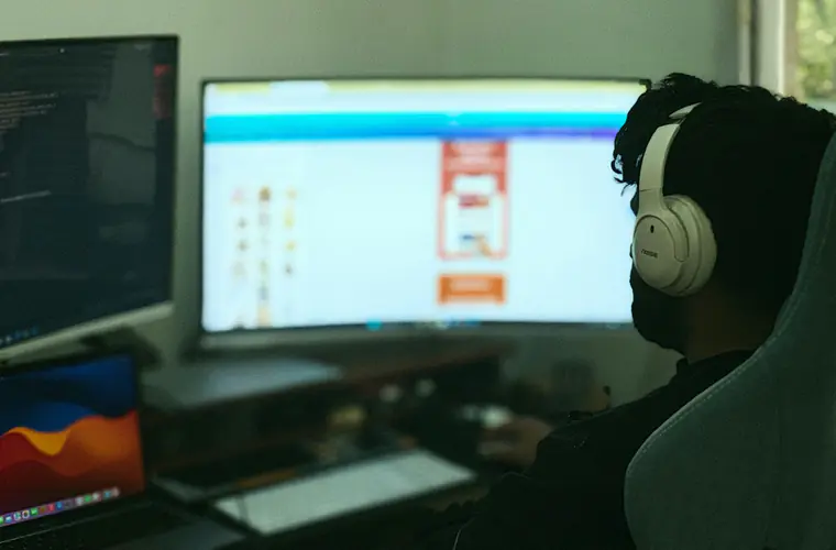 Developer at a two-screen desk, code open on the left monitor, working late.